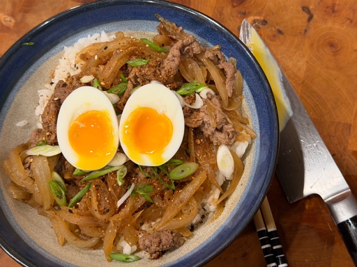 Simmered shaved beef and onion over a bed of rice, topped with a runny soft boiled egg.