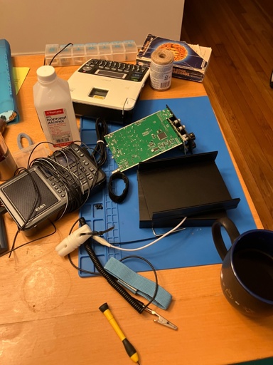 A wooden table is covered with radio related albums like a radio being taken apart and isopropyl alcohol. Other items from family life are visible on the table, like a coffee mug and an old copy of the Guinness Book of World Records.  